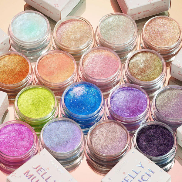 Totally Jelly ColourPop Full Collection Set showcasing 16 Jelly Much eyeshadow pots, lids off to reveal shimmery shades from mint and champagne to coral, lime, cobalt, lilac, and deep plum, arranged on a reflective peach surface with boxes nearby.