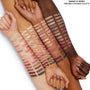 Total Smokeshow swatches sweep across four forearms from light to deep skin tones, showcasing cool neutrals, rosy pinks, and metallic shimmers, demonstrating pigment and blend of the ColourPop Shadow Palette & Brush Set with matching eye brushes.