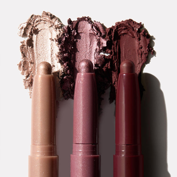 Three Rose Goals ColourPop Shadow Stix showcase creamy swatches - champagne shimmer, rosy mauve metallic, and deep burgundy - smeared behind the twist-up pencils on a white backdrop, highlighting the eyeshadow stick trio.