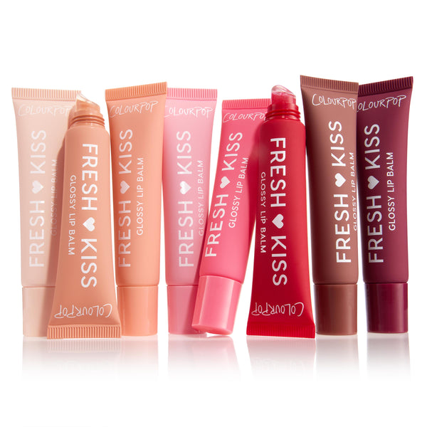 Eight Fresh Kiss Glossy Lip Balm tubes by ColourPop stand in a row, some uncapped to show slanted applicators, in nude, peach, pink, red, mauve, and plum shades on white; Gloss Goals Full Collection Set, a ColourPop Full Collection Set.