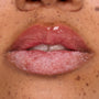 Glossy lips buffed with a candy cane sugar scrub while a hydrating mask coats the top lip, showcasing Colourpop Merriest Pout lip set in action, close-up on freckled skin to highlight smooth, exfoliated results.