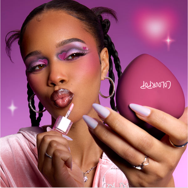 Model applies shimmery pink gloss while holding a heart-shaped senjyuan.onlinepact, showing bold purple and pink heart eye makeup that highlights the Heart to Get Full Collection full collection set against a dreamy pink background.