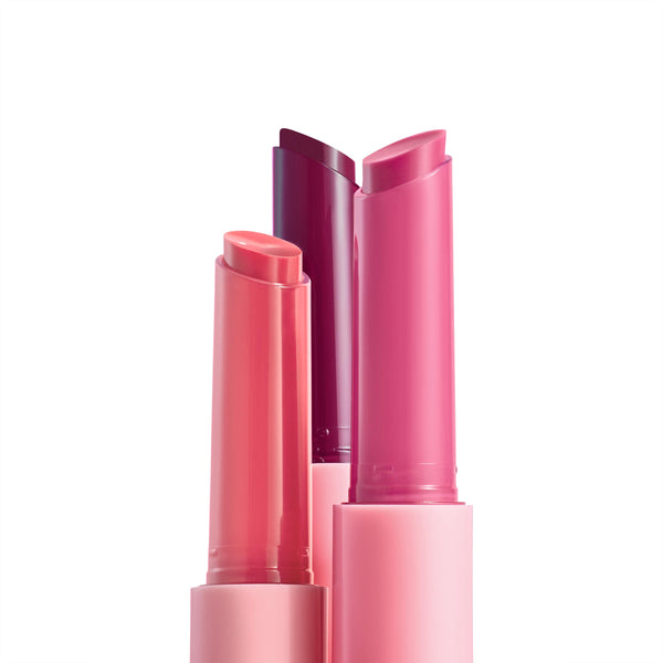 Trio of She’s So Juicy gloss balms stand uncapped - peach coral, bright pink, and deep berry - in pink tubes with angled bullets on a white background; ColourPop So Juicy Plumping Gloss Balm with Peptides set.