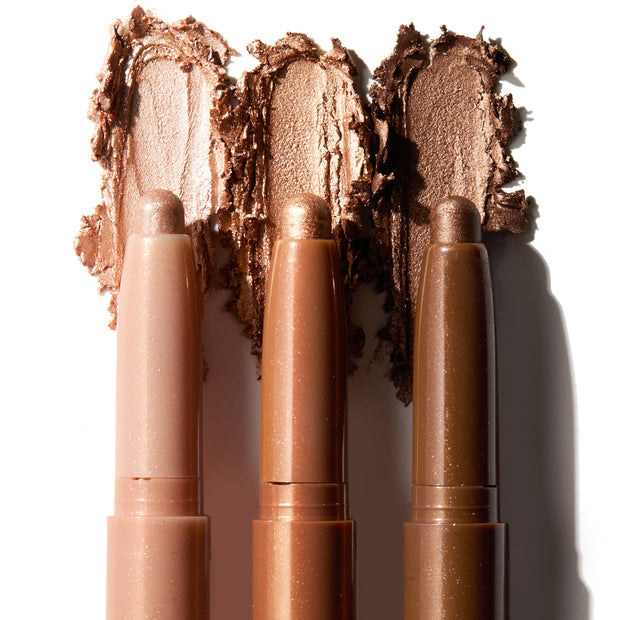 Three ColourPop Shadow Stix in Shimmering Golds glide swatches across a white background, revealing creamy metallic shades from champagne nude to warm gold to deep bronze in twist-up pencils for easy eye shadow application.