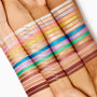 ColourPop Shadow Stix swatches on four arms, featuring the shade Cocktail Party labeled among rows of neutrals, brights, and shimmers; stacked stripes show color payoff across light to deep skin tones.