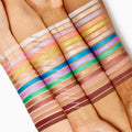 Shimmering gold Walk of Fame Shadow Stix swatch glows across three forearms, lined with other rainbow shades to show pigment and finish; ColourPop Shadow Stix displayed on light, medium, and deep skin tones for shade comparison.