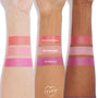 ColourPop Cream Blush Hypnosis swatched in a bold, cool fuchsia with a luminous sheen across three skin tones, positioned beneath coral Electroball and soft pink Metronome swatches on forearms against a white studio background.