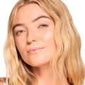 Glossy, sheer pink lips wearing ColourPop Fresh Kiss Glossy Balm in Vanilla Cake, showing a high-shine finish on a close-up model face with soft waves and natural makeup against a bright studio background.