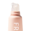 ColourPop Fresh Kiss Glossy Balm in Vanilla Cake dispensing a clear gloss bead from a slanted translucent applicator tip, shown in a macro close-up on a matte blush-pink tube against a clean white background.