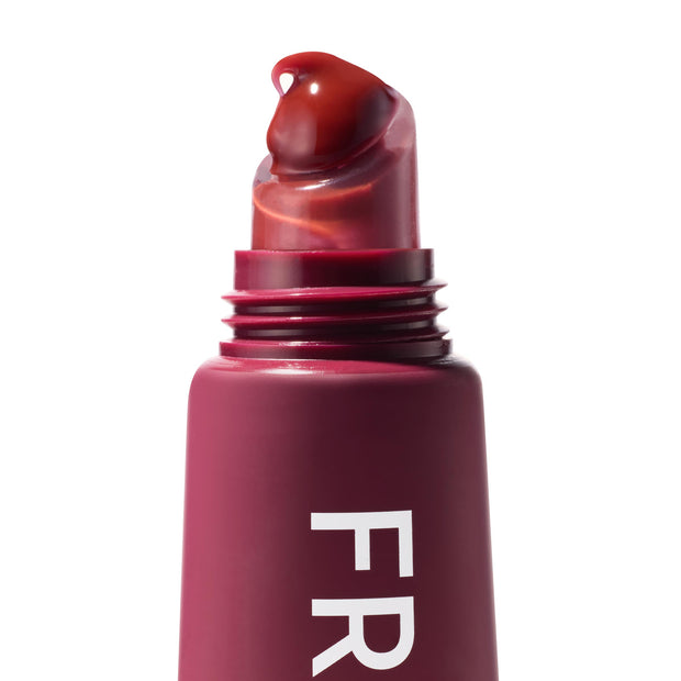 Wild Berry ColourPop Fresh Kiss Glossy Balm applicator releasing a droplet of rich berry gloss from a slanted clear tip, shown in a macro close-up with the maroon tube and partial FR lettering against a white background.