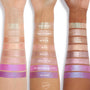 ColourPop Jelly Much Shadow in Duckling swatched in wide stripes on three skin tones, showing a metallic lavender-purple hue with blue iridescent shift; studio arm swatch lineup highlights pigment, shimmer, and payoff.