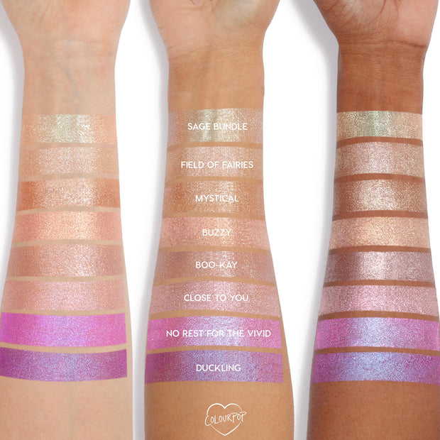 Buzzy Jelly Much Shadow swatched on three arms, showing a peachy rose-gold shimmer stripe among labeled shades; the ColourPop Jelly Much Shadow jelly-gel eyeshadow reflects metallic sparkle across light to deep skin tones.