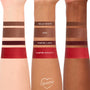 ColourPop Power Pout Lipstick Bella! Where the Hell Have You Been, Loca? swatches display four shades on three skin tones - Hello Biceps (deep brown), Jake (warm brown), Vampire Laws (oxblood), Vampire Royalty (vivid red) - stacked on forearms.