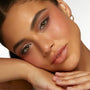 Neutral eye makeup showcasing Going Coconuts ColourPop Shadow Palette - soft taupe and cocoa shimmers on lids with defined lashes - model resting face on hands under studio light against a white backdrop, paired with peachy blush and nude gloss.
