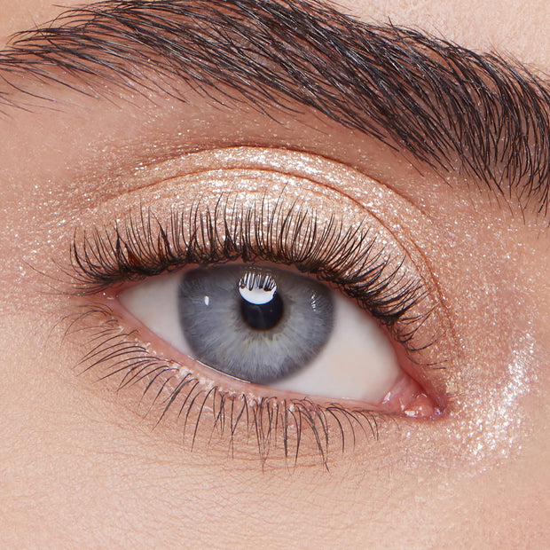 Ladybird Super Shock Shadow by ColourPop shimmering on eyelid - sparkly champagne-beige glitter eyeshadow swept across lid and inner corner for a metallic glow - shown in a close-up eye with long lashes and a defined brow.