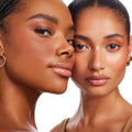 Two models showcase Manhattan Beach Bronzer Stix, wearing a warm sun‑kissed bronze with soft contour and dewy sheen; the ColourPop Bronzer Stix cream formula is smoothly blended on cheeks and temples in a clean white studio close‑up.