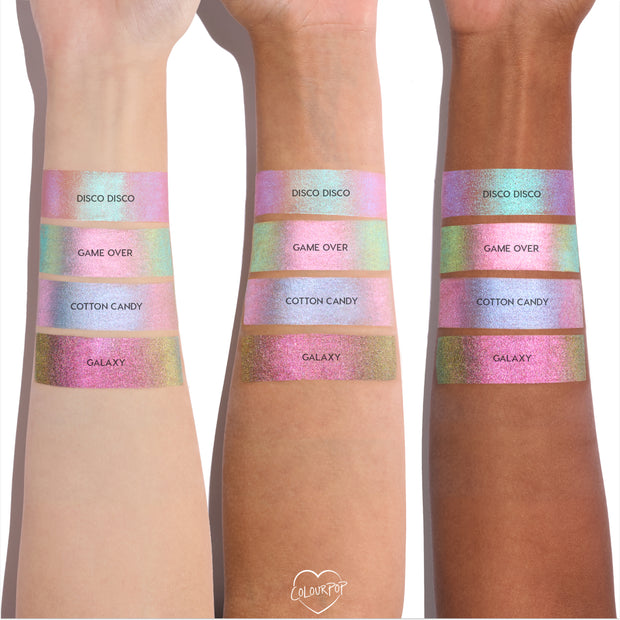 Colourpop Shadow Stix Game Over swatched on three skin tones, showing the shimmery pink-to-green duochrome strip labeled Game Over between Disco Disco and Cotton Candy shades on each forearm for comparison.