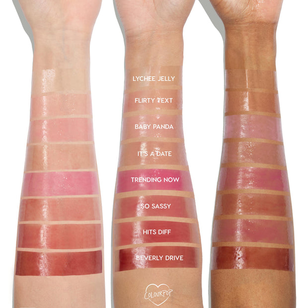Lychee Jelly swatched on three forearms from light to deep skin tones, a sheer glossy pink at the wrist among labeled shades, showcasing the shine and plumping payoff of the ColourPop So Juicy Plumping Glossy Lip Oil.