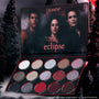 ColourPop Eclipse shadow palette from the Twilight collection lying open in a dark forest setting, showing 12 shimmer and matte cool-toned and red eyeshadows arranged in rows beneath moody character artwork on the inner lid.
