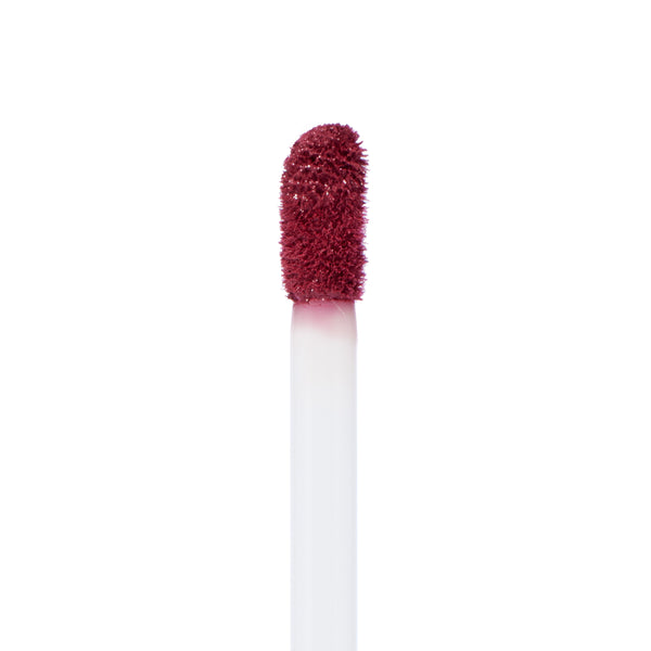 Doe-foot applicator coated in You Win Ultra Matte Lip, a deep berry red, showing velvety pigment and texture in macro on a white background; ColourPop Ultra Matte Lip wand ready for precise, long-wear application.