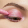 Juicy Gossip ColourPop Shadow Stix gliding over the eyelid, depositing shimmery bubblegum-pink color with a pearly finish; a tight eye close-up with natural brow showcases the creamy, blendable payoff.