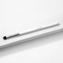 ColourPop Small Shader Brush makeup brush resting diagonally on a white textured surface, showing a sleek white handle with ColourPop logo, shiny silver ferrule, and dense flat rounded bristles for precise eyeshadow application.