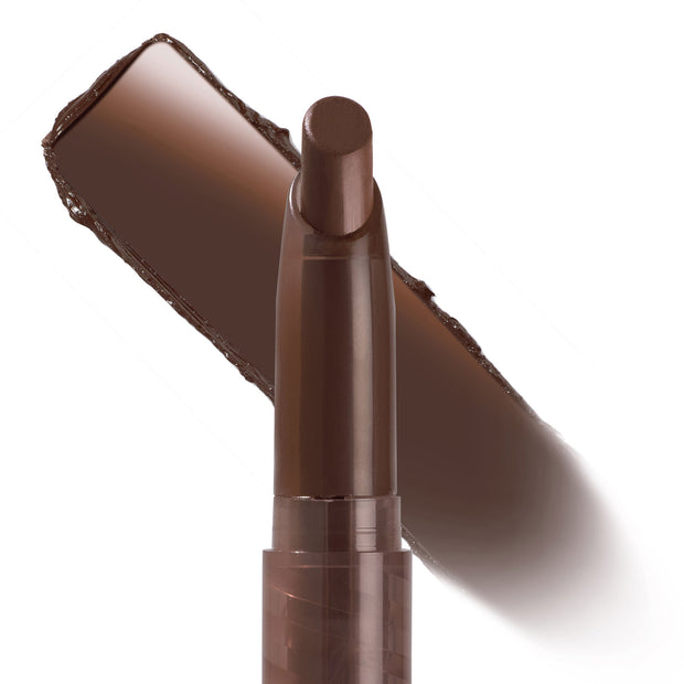 ColourPop Lippie Stix In the Nude standing upright with the bullet exposed, showcasing a deep brown nude lip color; a bold swatch streaked diagonally behind on a white background for shade reference.