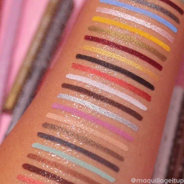 ColourPop Crème Gel Liner It’s a Vibe swatches bead water without smudging, with stacked lines of blue, yellow, gold, red, white, silver, black, and neutrals on a forearm, showing matte and metallic finishes against a pink vanity backdrop.